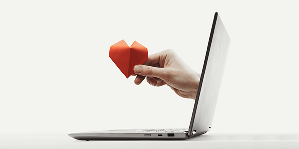 Laptop with a hand coming out of it offering a paper love heart as a pledge